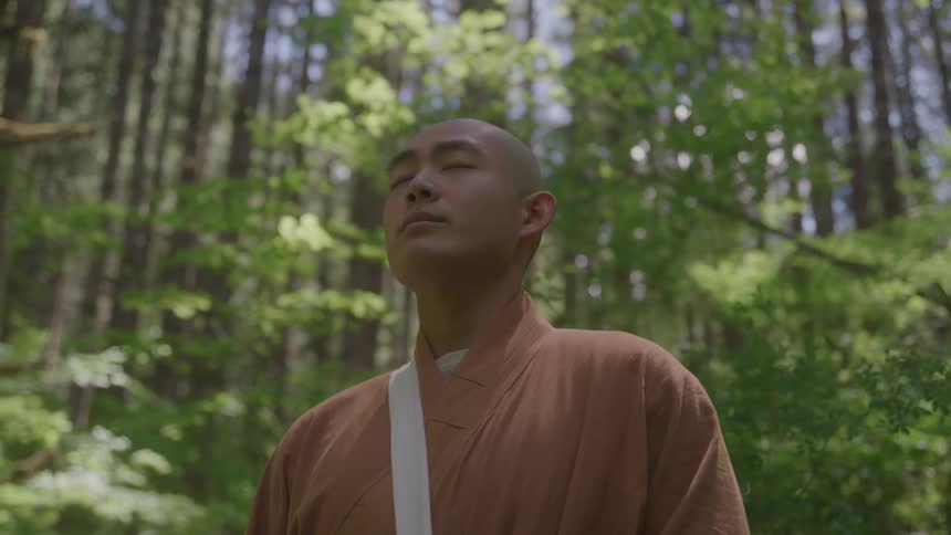Monk meditates standing in the forest with closed eyes