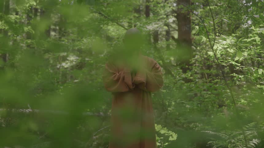 A person in traditional monk attire is praying in a green forest