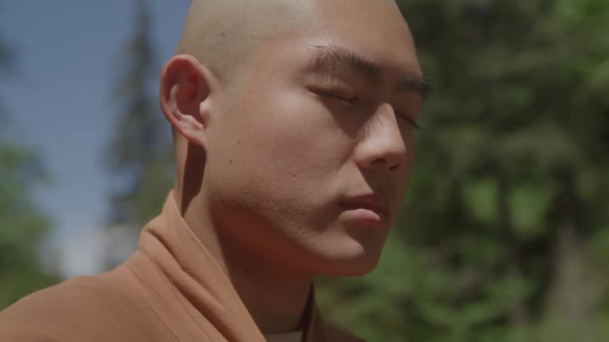 A monk sits outdoors meditating under the sun