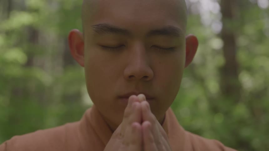 A male monk meditates with his eyes closed while outdoors