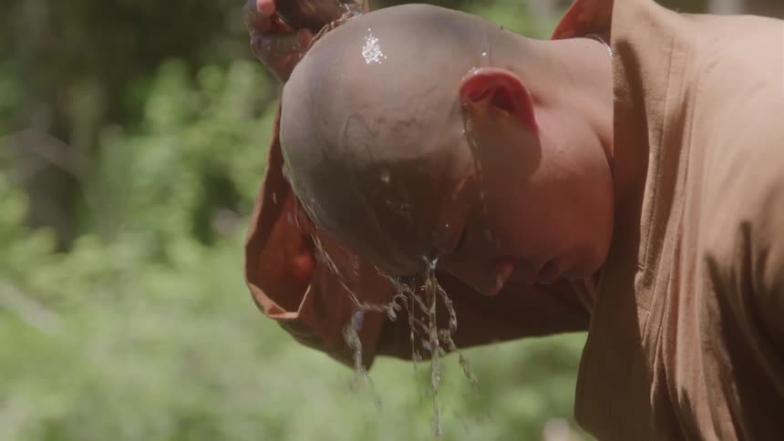 A buddhist monk using a bowl of water to wash his head