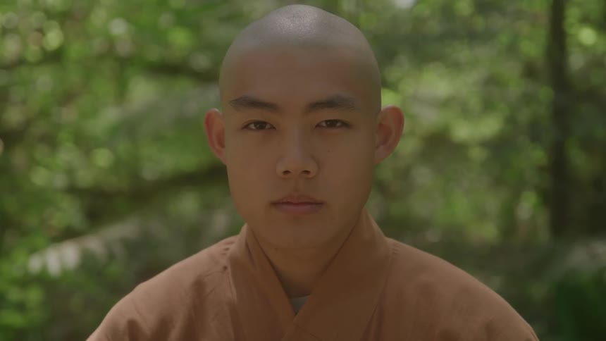 A bald person is looking directly at the camera they have a serious expression on their face