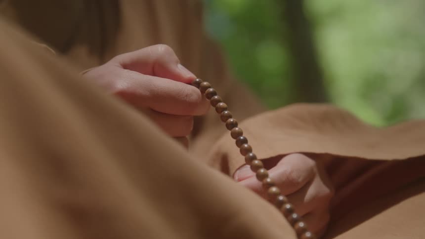 The video shows a closeup of a persons hands holding a string of brown prayer beads the persons thumb and fingers move the beads suggesting they are using them for meditation or prayer