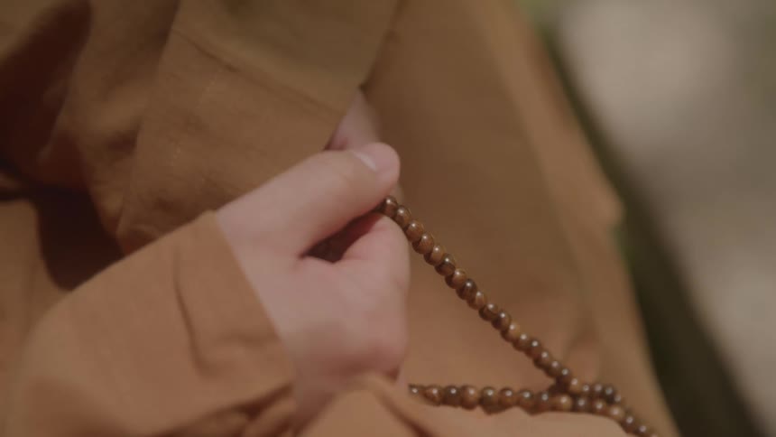 Hand holds a wooden bead rosary over a brown robe
