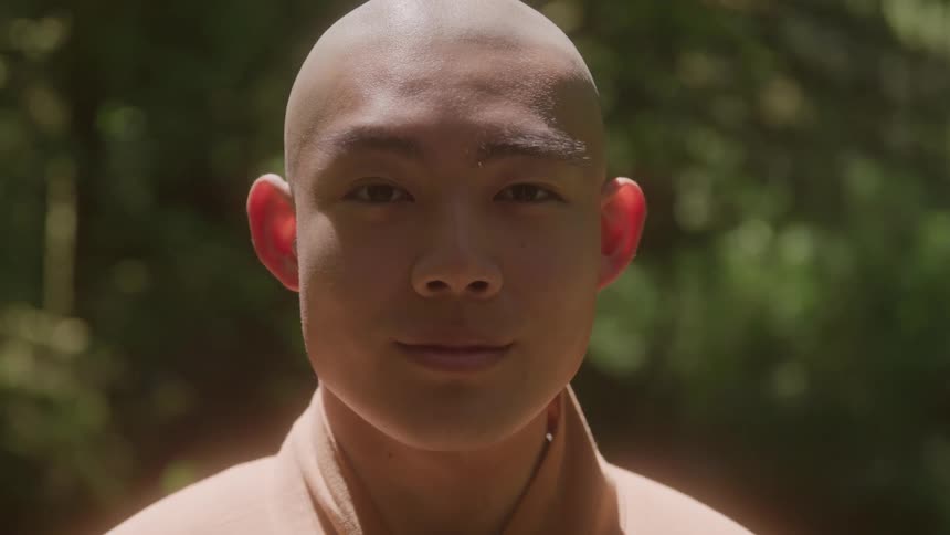 A young bald monk sits under the sun at midday