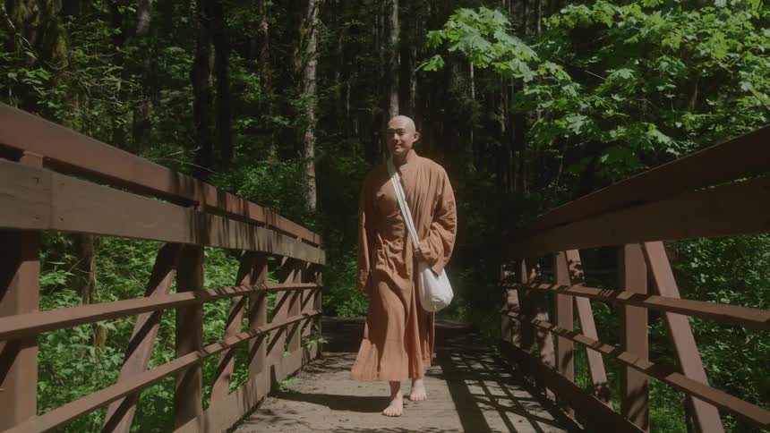 Monk walks barefoot across a wooden bridge in the forest