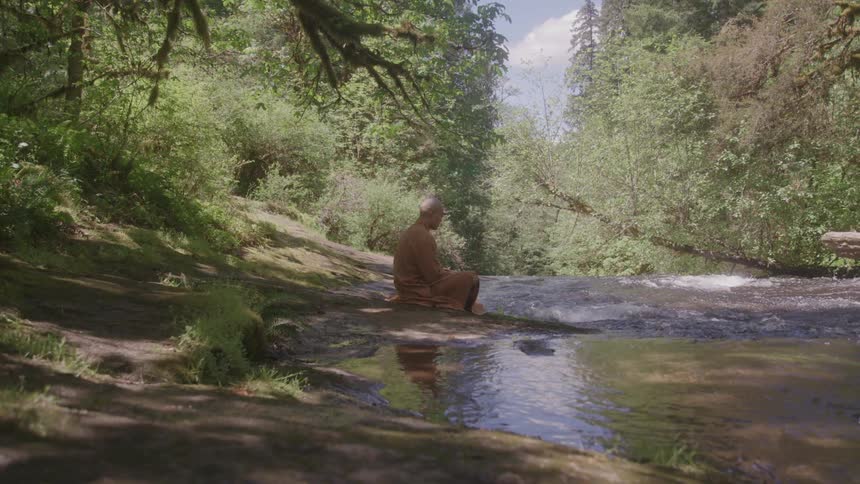 A buddhist monk meditating by a forest creek