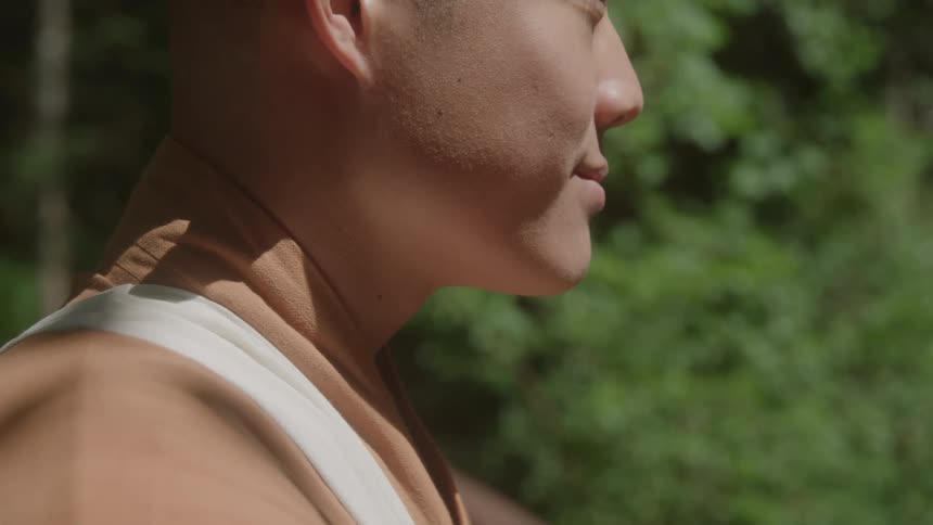 Young man in profile wearing light brown clothing in a natural setting