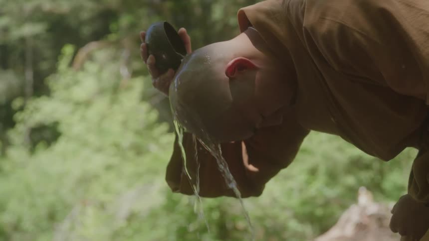 Monk pours water over his head in the midst of nature