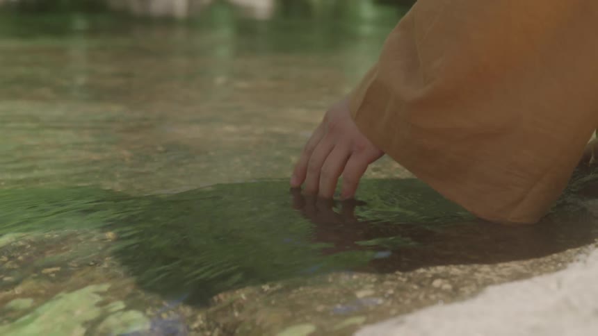 A person dips their hand in the stream water