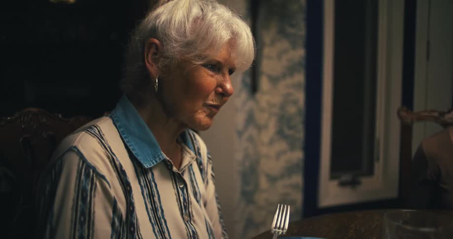An elderly woman sitting at a table eating with a young woman nearby