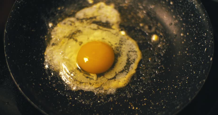 Hands cracking a brown egg over a hot frying pan