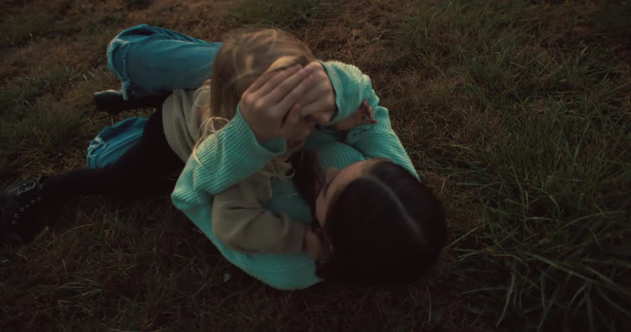 A teenage girl picking up a young girl in her arms and gently dropping her onto the grass while playing