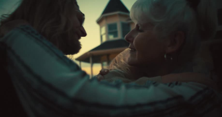 A woman with white hair is hugging a man with long hair the woman is smiling