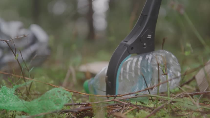 Instrument picking up discarded plastic bottle on the forest floor among branches and leaves