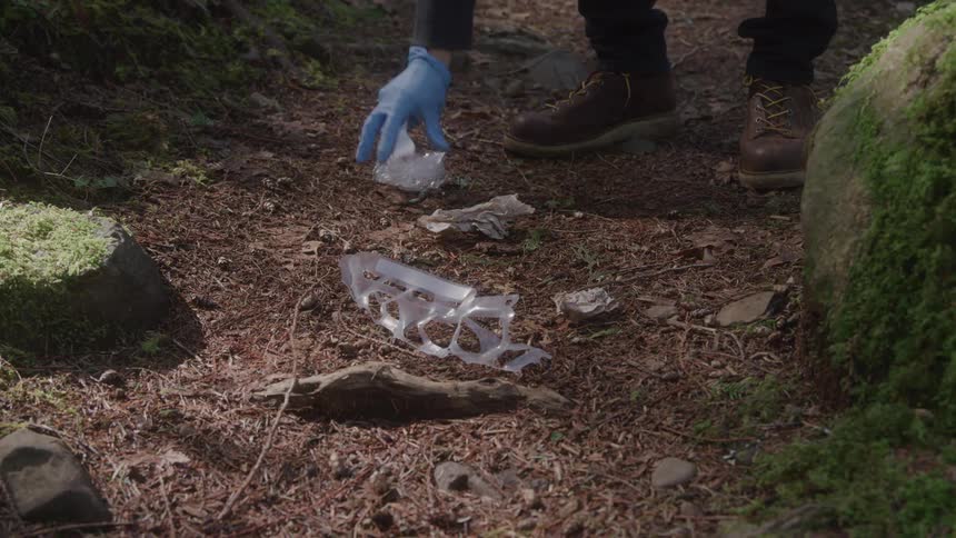 Person wearing blue gloves picks up plastic trash on a forest trail
