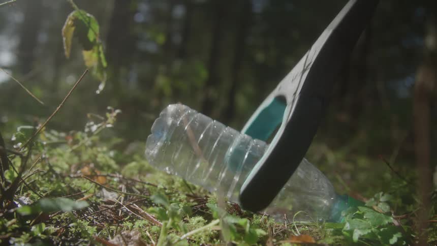 A tool picks up plastic bottle from forest floor