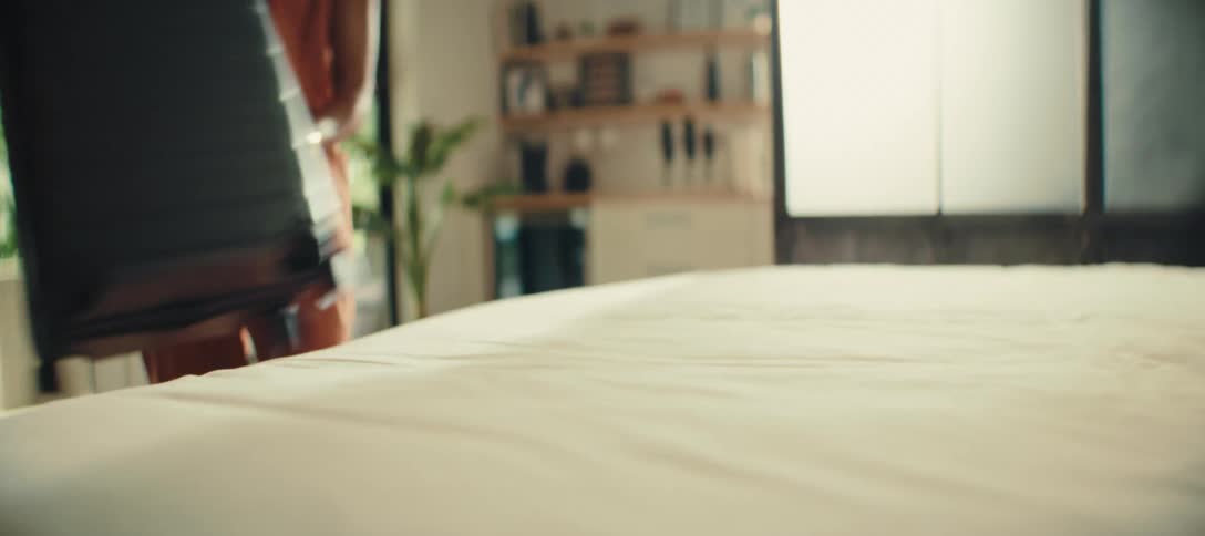 A person is pulling a black suitcase off of a bed the suitcase is then placed on the floor