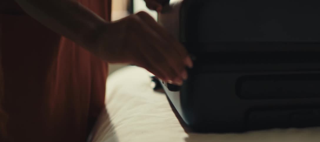 Hand closes the zipper of a black suitcase on the bed