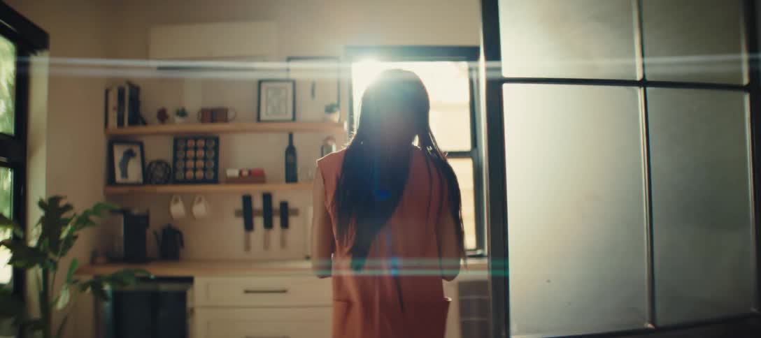 Woman standing in a sunlit kitchen looking at the watch on her wrist