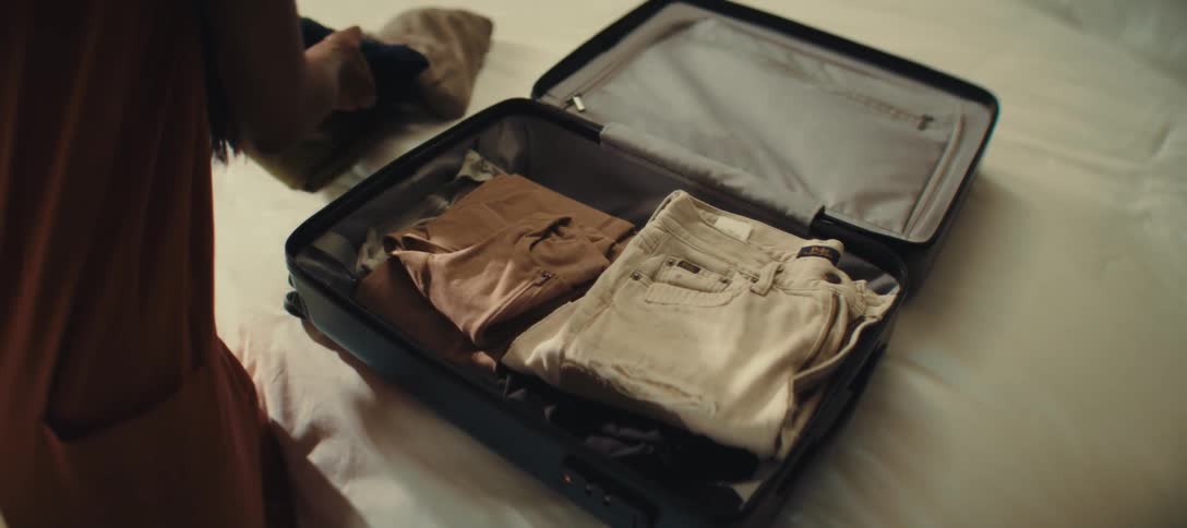 A woman opening a suitcase and putting clothes inside