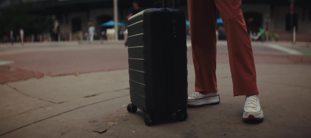 Woman standing with her luggage as pedestrians pass by in the distance