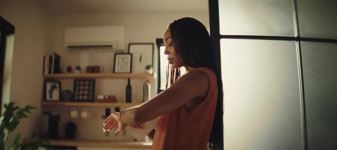 A woman standing inside her house using her phone and then checking the time on her wristwatch