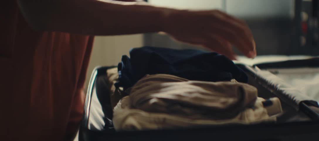 While packing woman adjusts her clothes in her suitcase then closes it