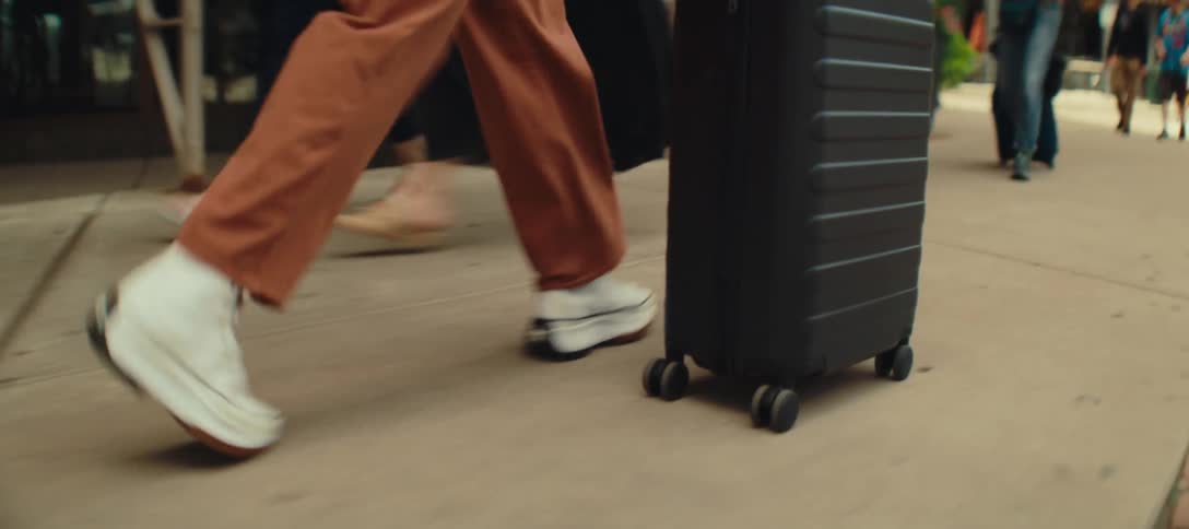 A woman rolls her luggage on the sidewalk