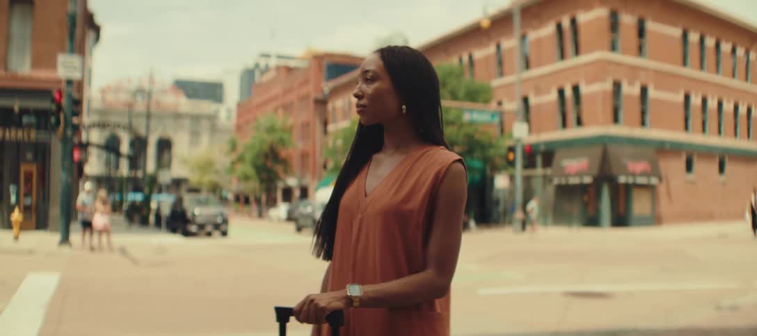 A woman stands by the intersection with her luggage