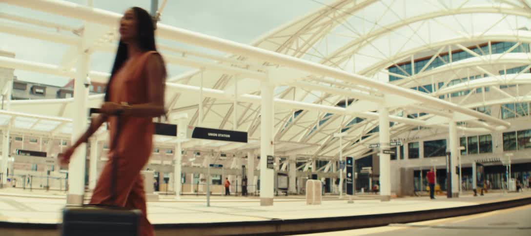 Woman with rolling suitcase waits at a modern bright station