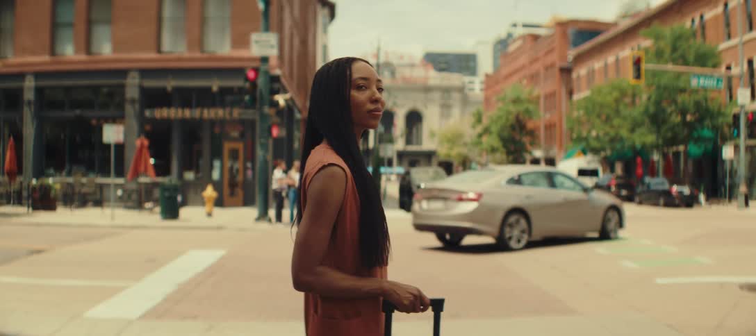 Woman crosses a busy street pulling a rolling suitcase