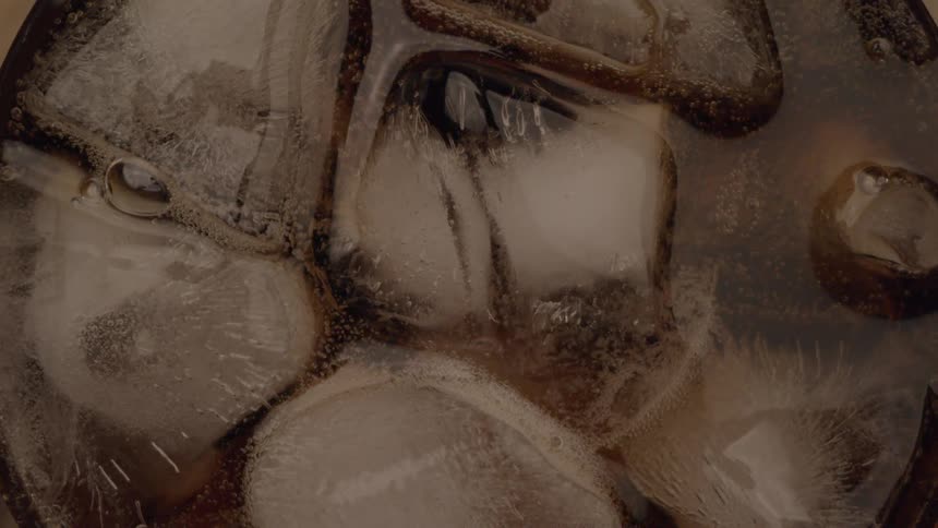 Extreme closeup of ice cubes floating in a dark soda drink