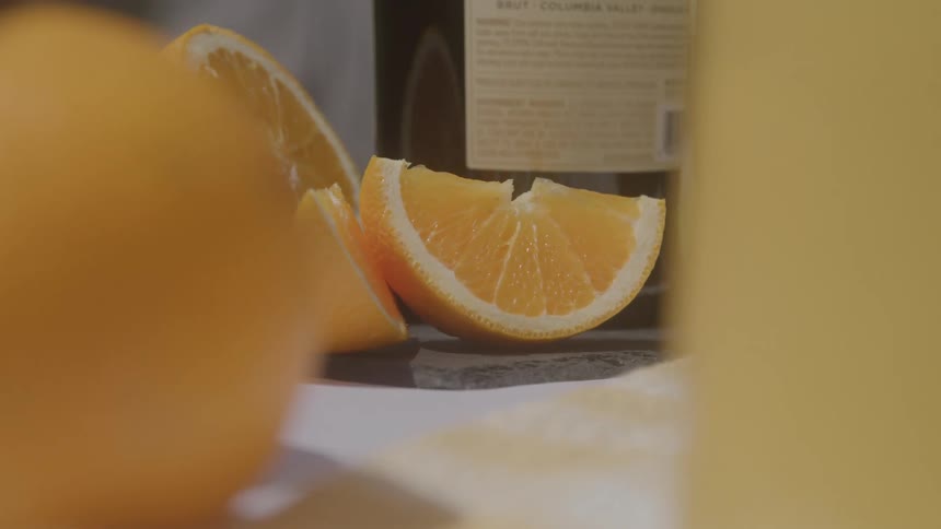 Based on the images from the video the scene shows a closeup of several orange slices and a whole orange on a surface in the background there are blurred bottles of what appear to be wine or spirits the camera pans slowly to the right revealing more