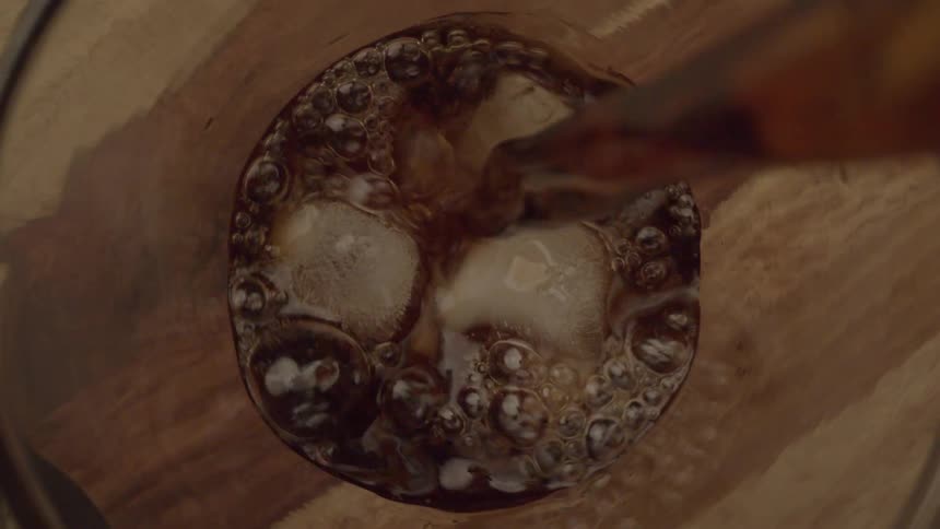 A drink is poured into a glass with ice cubes