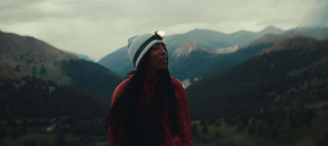 Person wearing a beanie and headlamp looks at the mountainous landscape at dusk