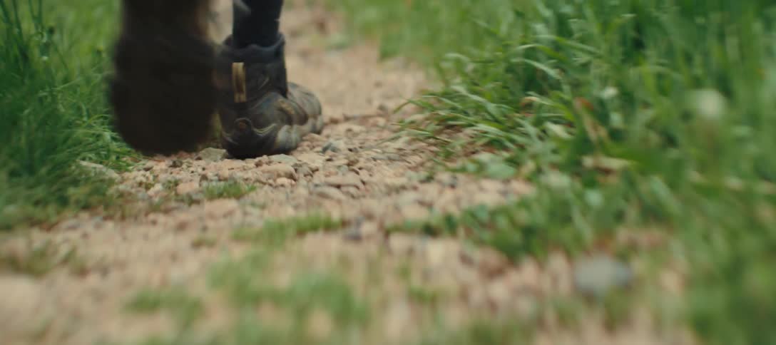 A man walks forward on a dirt trail wearing black socks and shoes