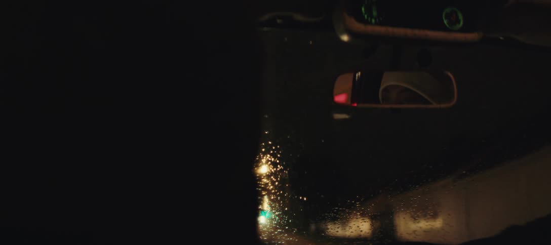 Rainy night car scene with the drivers eyes visible in the rearview mirror