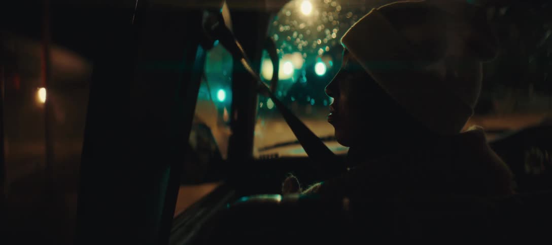 The woman is looking through the water covered windows of the moving car