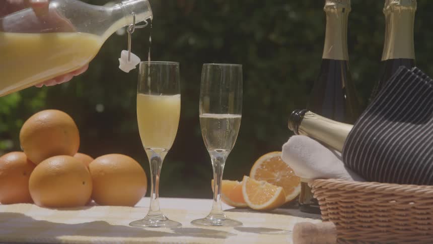 Hands pouring orange juice into flutes