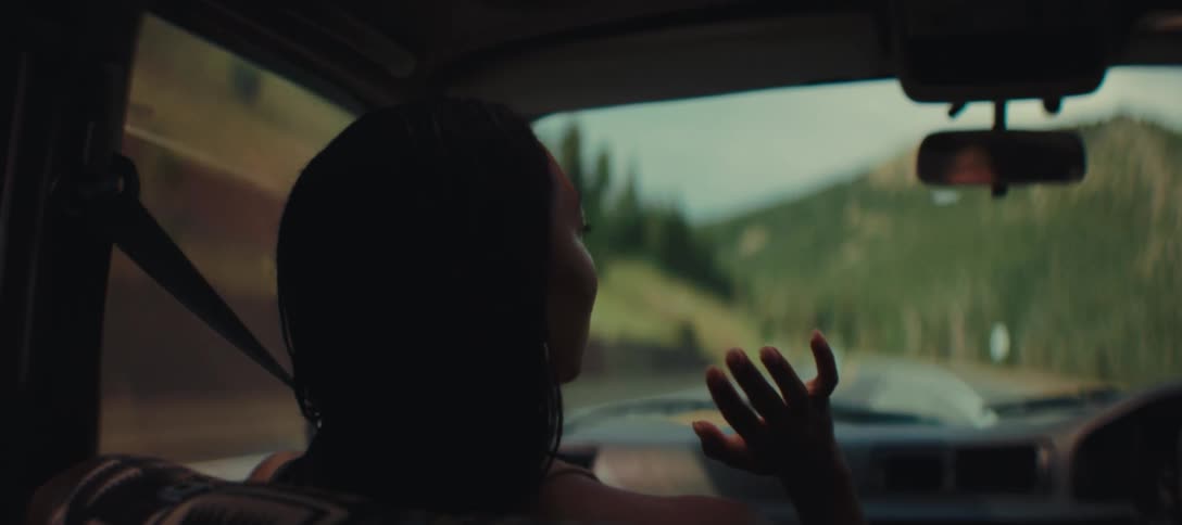 Woman in the passenger seat raises her hand as the car drives along a mountain road