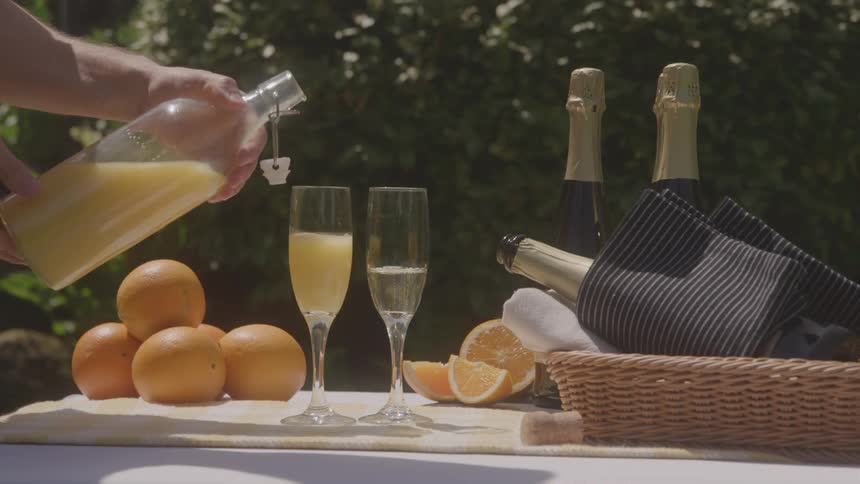 A hand pours orange juice into champagne glasses outdoors