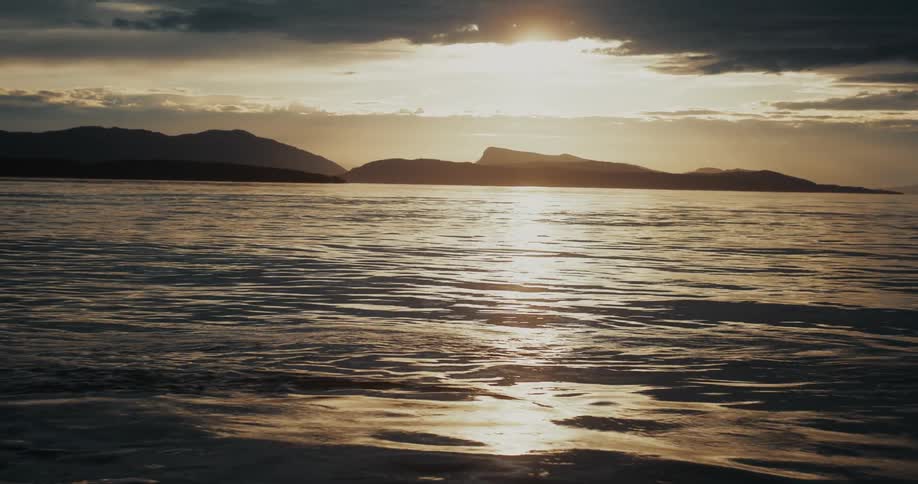 Sunlight reflects on the ripples and waves in the water with mountains along the coast