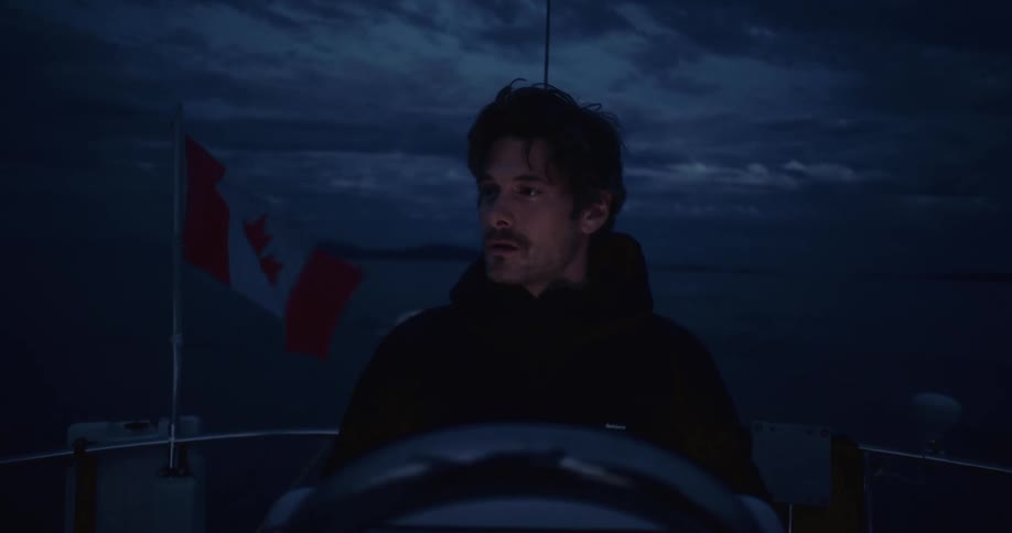 Man steers a boat at night with the canadian flag in the background