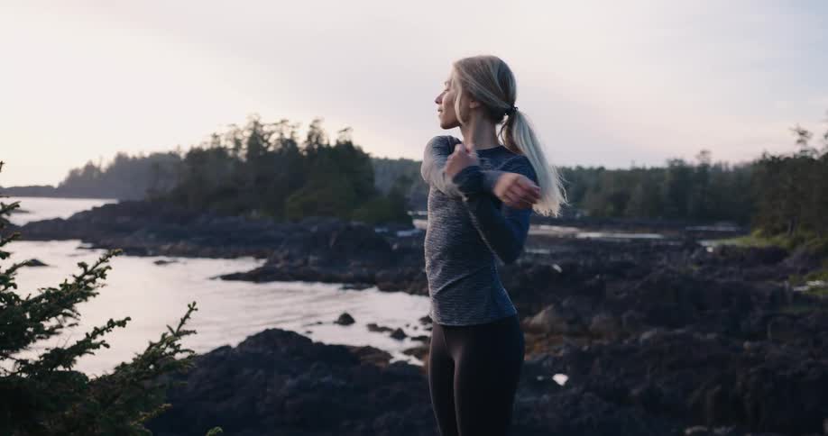 Woman stretches by a rocky coastline