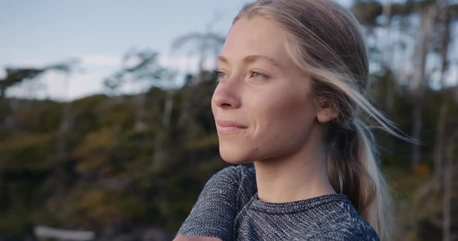 Blonde woman smiles and stretches while standing outdoors on a windy day