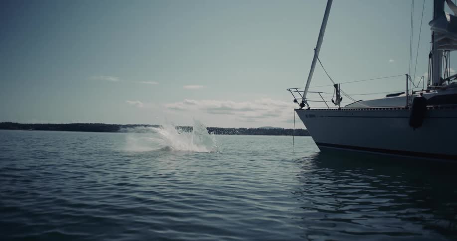 Person dives into the sea beside a sailboat