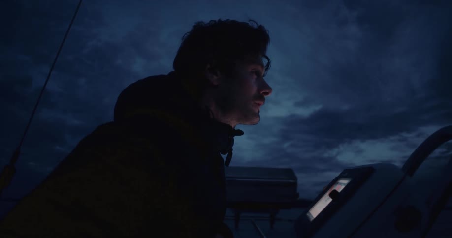 Man steers a boat at night under a cloudy sky