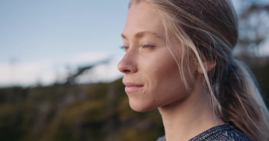 Based on the images from the video a closeup portrait of a woman with long lightcolored hair is shown she is looking off to the side with a serious thoughtful expression the background is blurred but appears to be a natural setting with some green