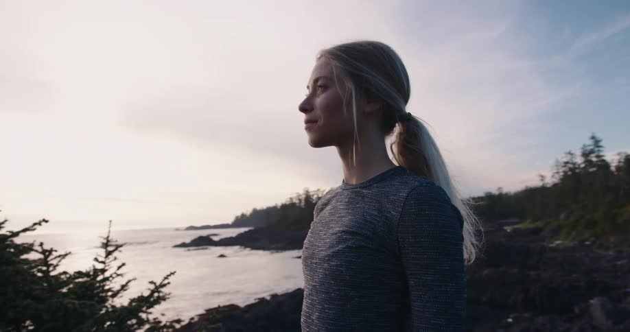 A woman looks out over a rocky coastline at sunset